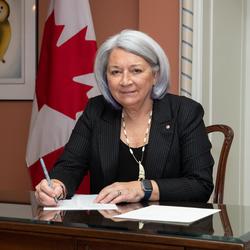 La gouverneure générale, assise à une table, signe un document.