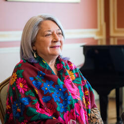 La gouverneure générale Mary Simon est assise. Elle porte un magnifique foulard multicolore. Un piano est visible à l'arrière-plan.