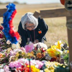 La gouverneure générale Mary Simon dépose quelque chose sur un monticule de fleurs. Il y a une croix floue au premier plan.