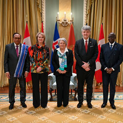Governor General Simon and four heads of mission, with the flags of each country behind them. Two Ceremonial Guards are in the back.