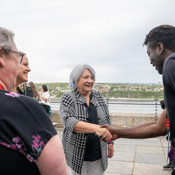 Governor General Mary Simon shaking hands with a person. Other people are standing around. They are all outside.