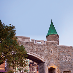 Un arc aménagé dans un ancien mur de pierre débouche sur une rue du Vieux-Québec. Une tourelle à toit vert se dresse au sommet du mur.