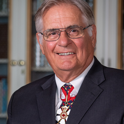 Official photo of His Excellency Whit Grant Fraser. Bookshelves are visible in the background.