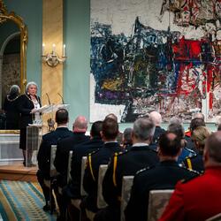 Governor General Mary Simon speaks at a podium in the ballroom at Rideau Hall. She is looking out at a crowd of recipients of the Order of Merit of the Police Forces. The recipients are wearing police uniforms. 