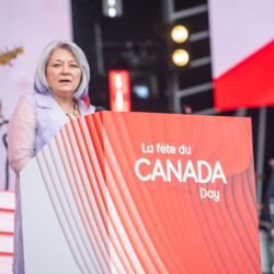 La gouverneure générale prononce un discours à partir d'un podium. Le podium dit " La fête du Canada/Canada Day ".