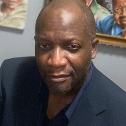 Member of the Order of Canada - Robert Small. He is wearing a dark shirt and suit jacket. Painted portrait are visible behind him.