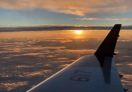 View of airplane wing from inside a plane with the sun setting.
