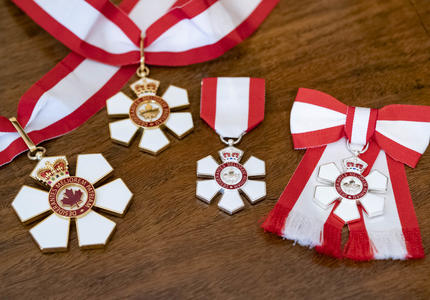 Four insignia of the Order of Canada. The insignia of the Order is a stylized snowflake of six points, with a red annulus at its centre which bears a stylized maple leaf circumscribed with the motto of the Order. 