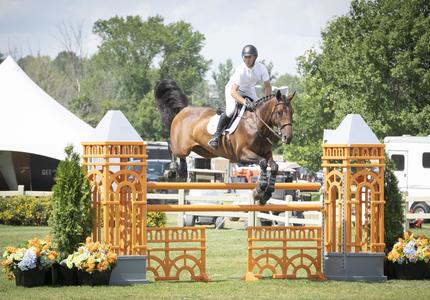 A rider and his horse jump over a fence during an outdoor equestrian competition.
