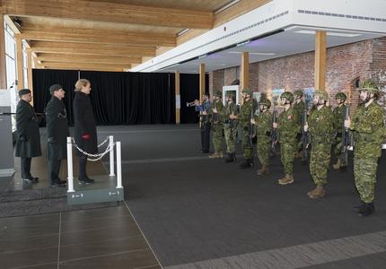 Governor General Julie Payette is standing on a dais and looks at an Honour Guard of two rows of 8 reservists in combat uniform.