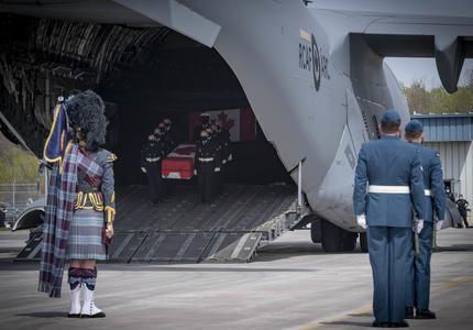 CAF members, including a bagpiper watch as a coffin, carried by CAF members, is taken off a plane.