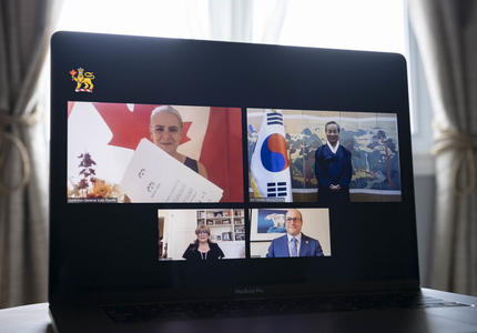A computer screen split in 4 rectangles with a person in each one, 2 women and 2 men. Top left rectangle shows a Canada flag behind a woman, holding a certificate-like paper. On her right, a man is standing next to the Korea flag.