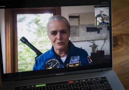 A woman in a blue space flight suit is shown on an open laptop screen.