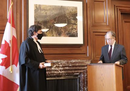 Chief Justice Richard Wagner holding a book. Ian Shugart - clerk of the Privy Council of Canada - stands a podium. 