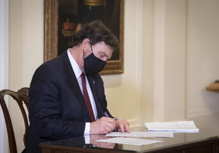 The Administrator sitting at a table, signing a document.