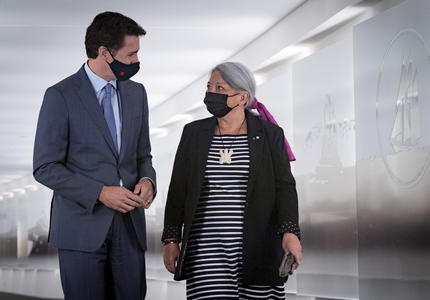Le premier ministre Justin Trudeau et la gouverneure générale désignée Mary May Simon marchent dans un couloir côte à côte en se regardant.