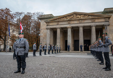Large building in the background. Members of the German military are standing in uniform. They are outdoors.