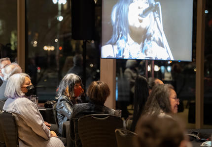 Audience, including Governor General Mary Simon and Buffy Sainte-Marie, watching a video screen of a Buffy Sainte-Maire performance.