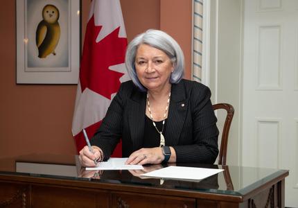 La gouverneure générale, assise à une table, signe un document.