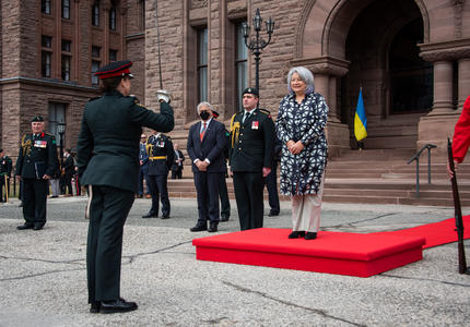 Governor General Simon is standing on a red podium outside of Queen’s Park.
