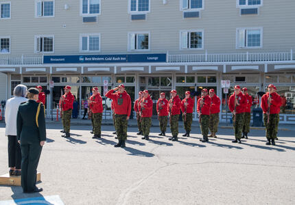 La gouverneure générale Simon est debout sur une petite plateforme légèrement surélevée. Une femme portant un uniforme militaire se trouve derrière elle, à sa droite. Elles font face à une garde d'honneur composée de Rangers canadiens.