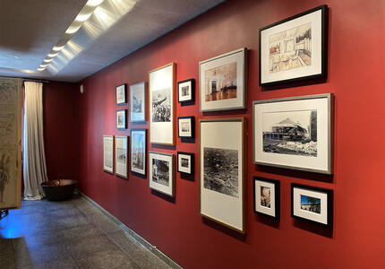 Vue en angle à droite d'un mur rouge qui présente un mélange de 17 photographies, croquis et peintures sur un mur rouge.