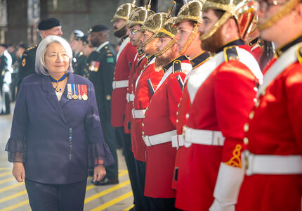 La gouverneure générale Mary Simon, portant un complet violet et des médailles militaires, marche devant une garde militaire portant des uniformes rouges.
