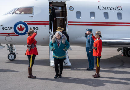 La gouverneure générale Mary Simon marche à l'extérieur. Un avion se trouve derrière elle.