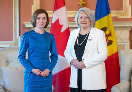Governor General Mary Simon stands next to Moldovan President Maia Sandu at Rideau Hall. Both women are smiling. A Canadian and Moldovan flag can be seen behind them. 