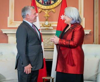 Governor General Mary Simon, wearing a red vest, is facing and talking to the King of Jordan, wearing a grey vest and purple tie. 