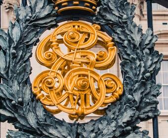 Black wrought iron gates mounted with golden detailing and a crest of a wreath with gold lettering, surmounted by a crown. 