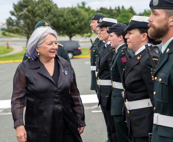 La gouverneure générale Simon passe devant une rangée de personnes en uniforme. Ils sont dehors.