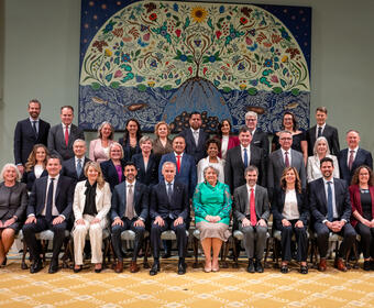 Governor General Simon and Prime Minister Mark Carney sit in the front row of a group photo in the ballroom at Rideau Hall. They are surrounded by members of the new Canadian Ministry.
