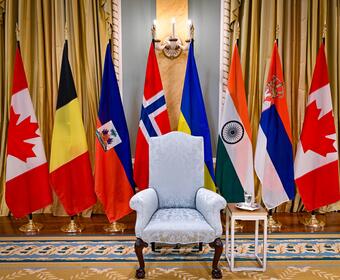 A regal chair flanked by flags from Belgium, Haiti, Norway, Ukraine, India, and Canada. They are displayed indoors.