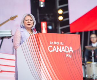 La gouverneure générale prononce un discours à partir d'un podium. Le podium dit " La fête du Canada/Canada Day ".