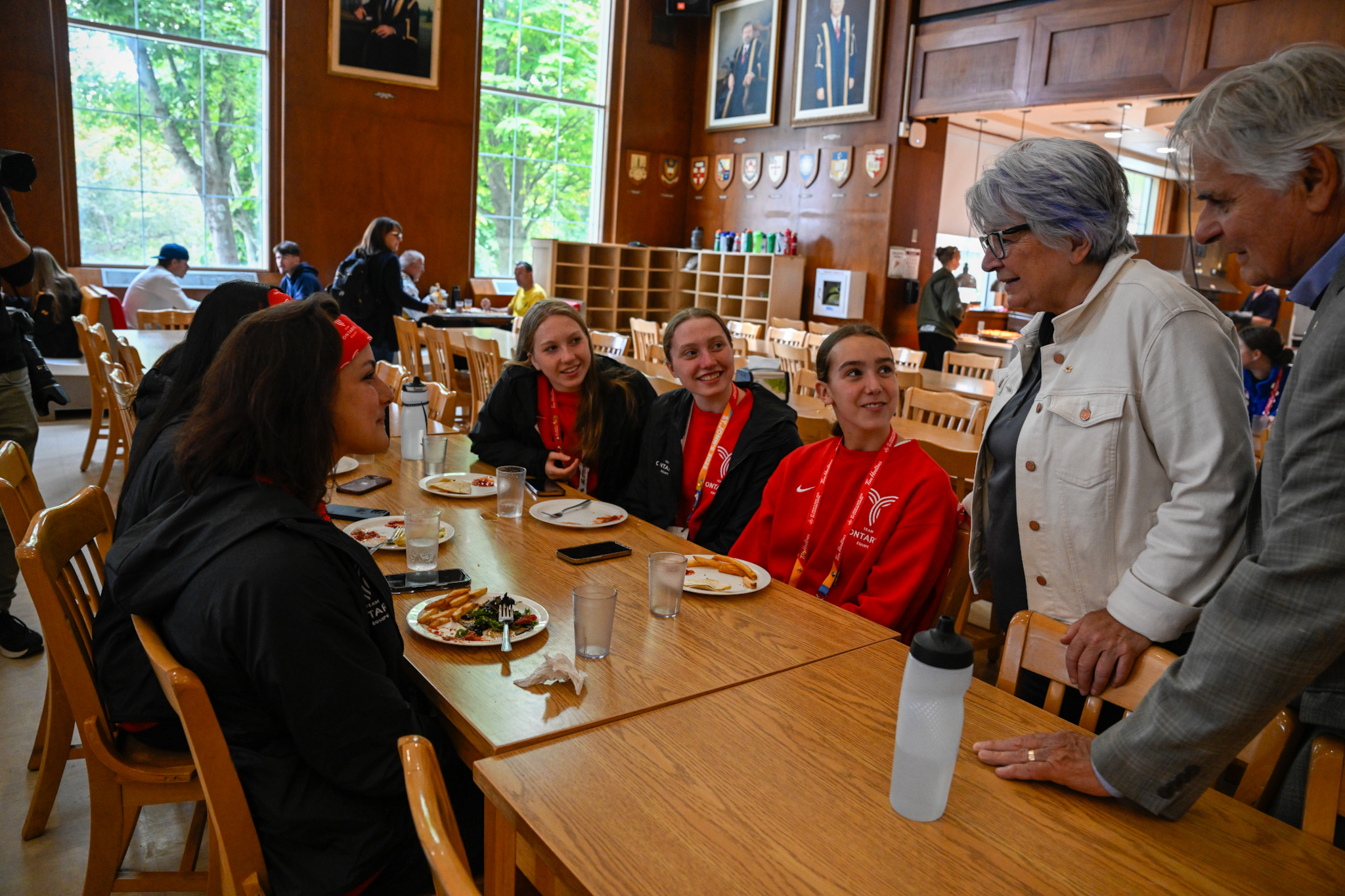 La gouverneure générale Mary Simon et M. Whit Fraser debout, discutant avec un groupe de personnes qui prennent leur petit-déjeuner autour d'une grande table.