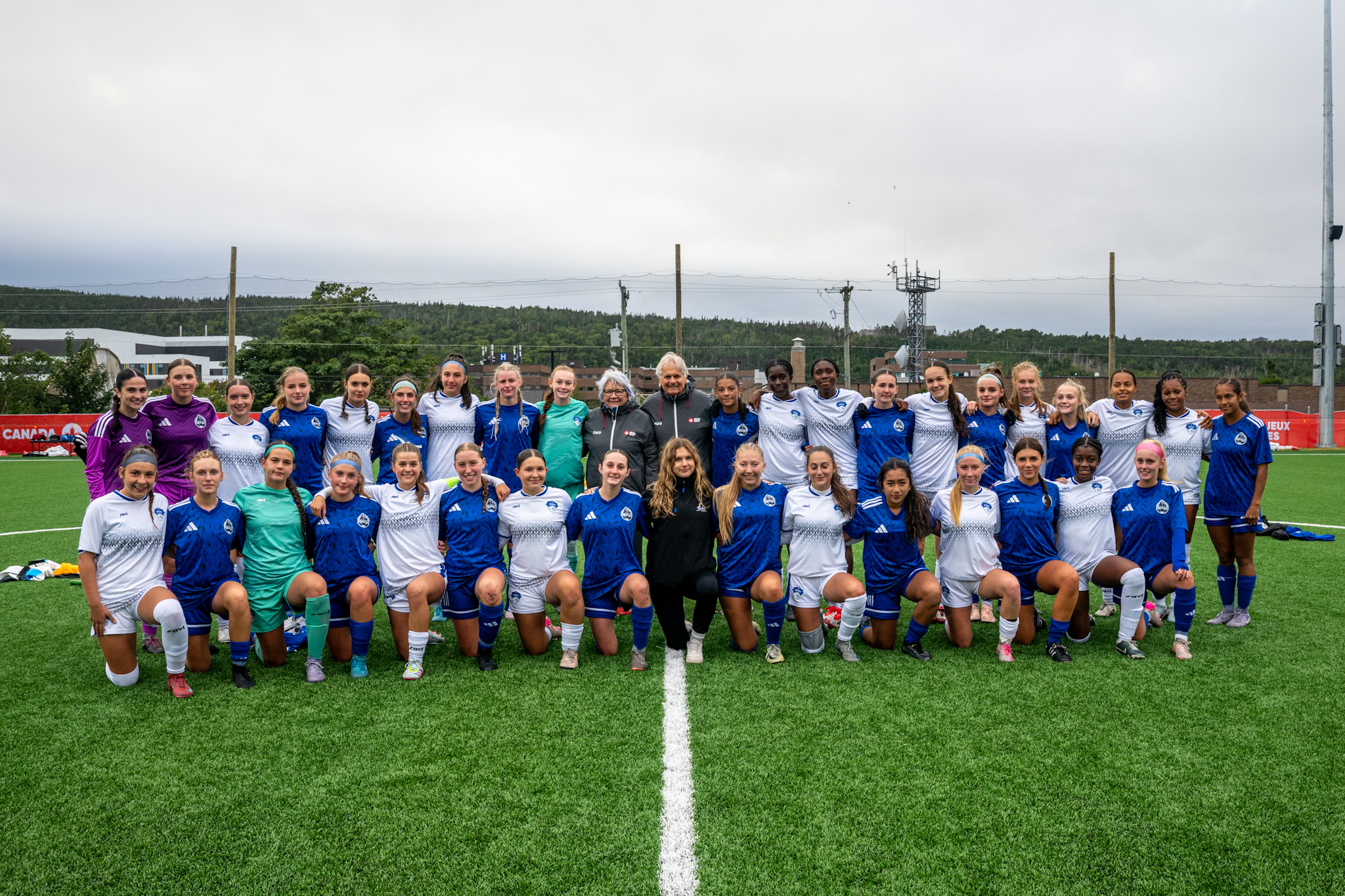 Photo de groupe d'une équipe de football posant sur le terrain. La gouverneure générale Mary Simon et M. Whit Fraser se tiennent au milieu du groupe.