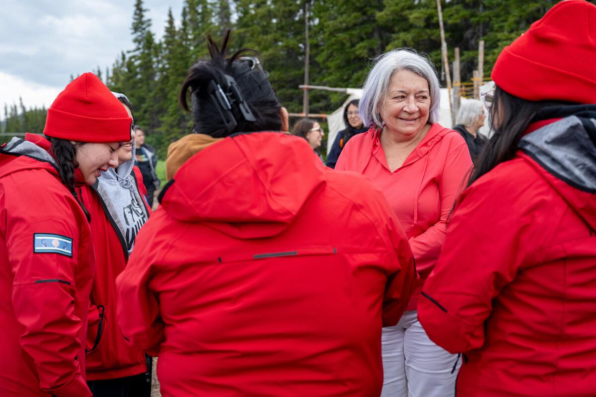 Governor General Mary Simon is chatting with a group of students dressed in red. They are outside.